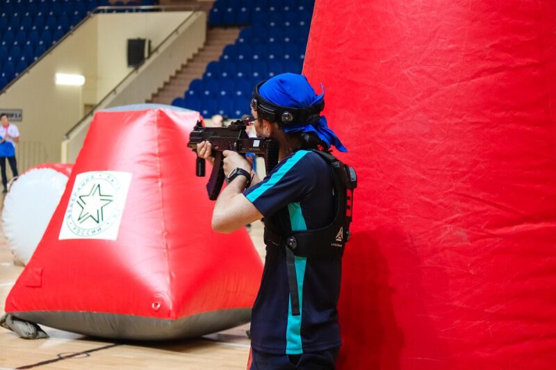 Игрок LASERWAR с оружием за красным укрытием прицеливается.